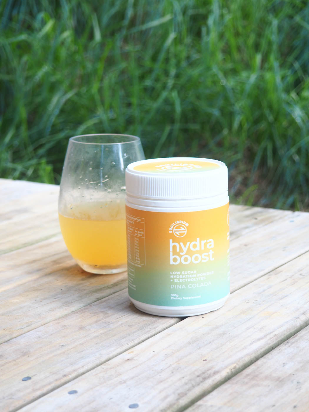 Equilibrium Nutrition Hydra Boost tub with a mixed drink on a rustic wooden surface.